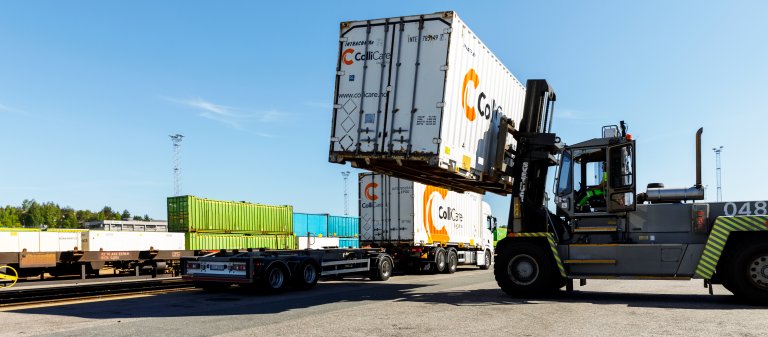 A white container is loaded from a train wagon on to a truck trailer by a forklift.