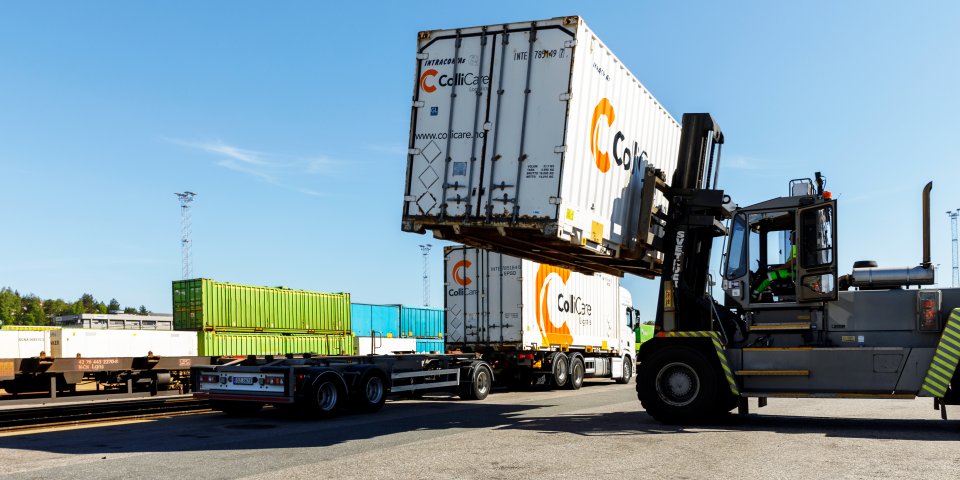 A white container is loaded from a train wagon on to a truck trailer by a forklift.