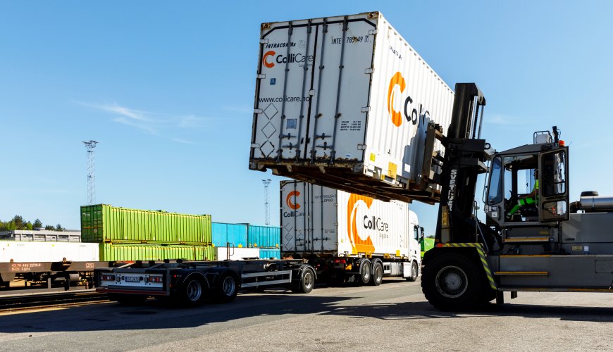 A white container is loaded from a train wagon on to a truck trailer by a forklift.